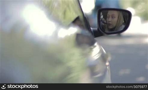 Closeup of male hand opening car door. Background reflection of beautiful woman in car&acute;s side view mirror doing makeup in passenger seat