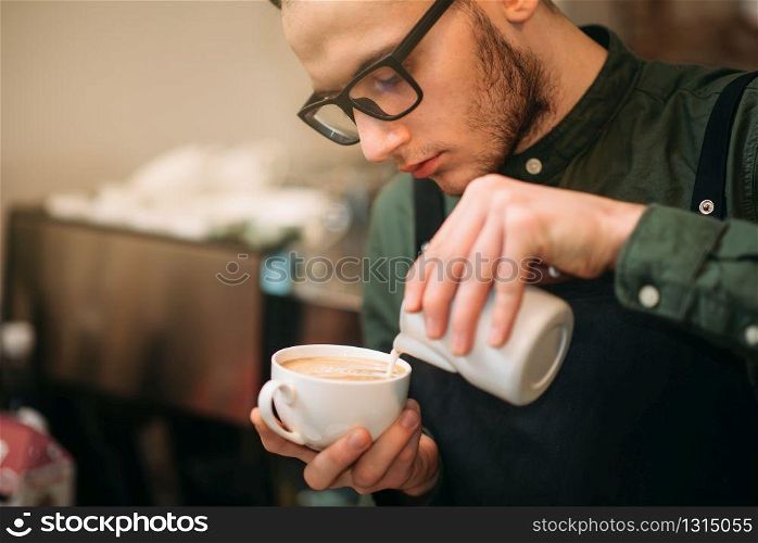 Closeup of male hands adding cream to coffee. Blur table, plate and spoon on the background.. Closeup of male hands adding cream to coffee.