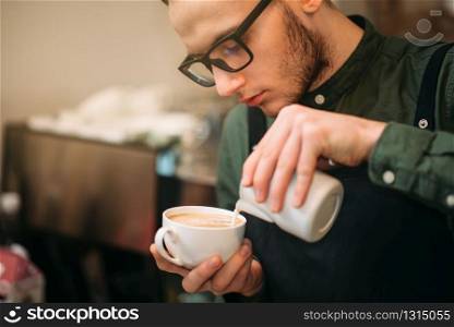 Closeup of male hands adding cream to coffee. Blur table, plate and spoon on the background.. Closeup of male hands adding cream to coffee.