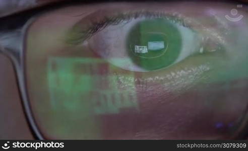 Closeup of man&acute;s eye in glasses works on laptop at night. Macro young man in glasses surfing on Internet