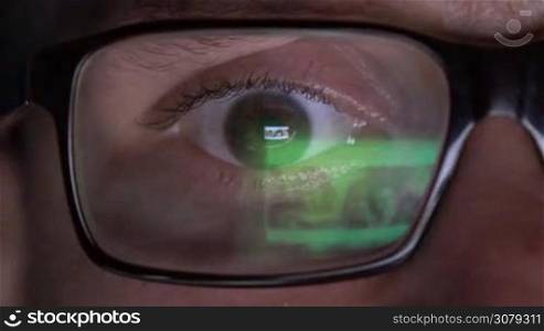 Closeup of man&acute;s eye in glasses works on laptop at night. Macro young man in glasses surfing on Internet