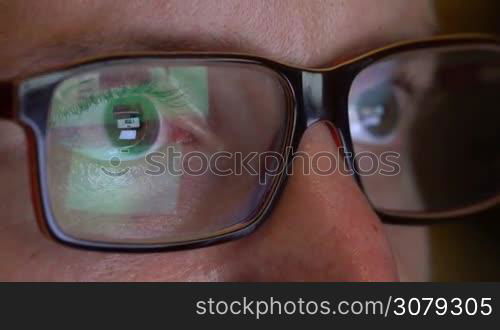 Closeup of man&acute;s eyes in glasses works on laptop at night. Macro young man in glasses surfing on Internet