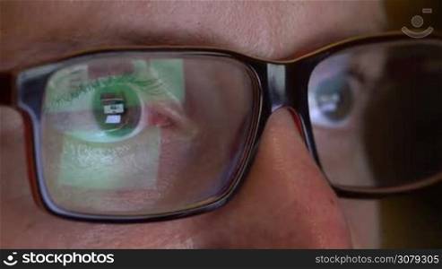 Closeup of man&acute;s eyes in glasses works on laptop at night. Macro young man in glasses surfing on Internet