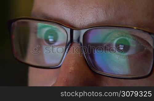 Closeup of man&acute;s eyes in glasses works on laptop at night. Macro young man in glasses surfing on Internet