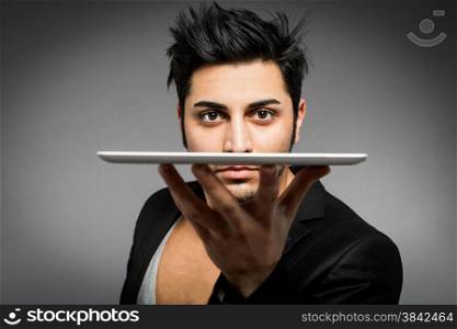 Closeup of man holding tablet pc on one hand in front of his face over grey background