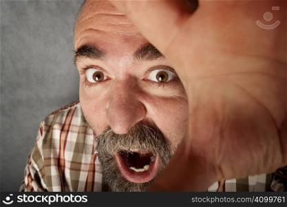Closeup of man in his forties with mustache screaming and fending off the camera
