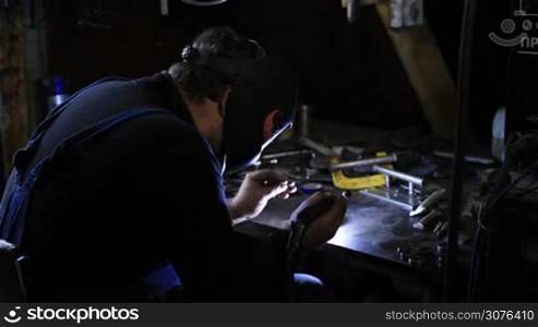 Closeup of man wearing mask welding in workshop. Welding steel using TIG welder. Back view.