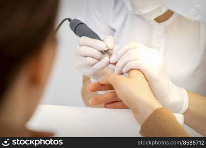 Closeup of manicure master removes nail polish uses an electric nail file in a nail salon. Manicure master removes nail polish