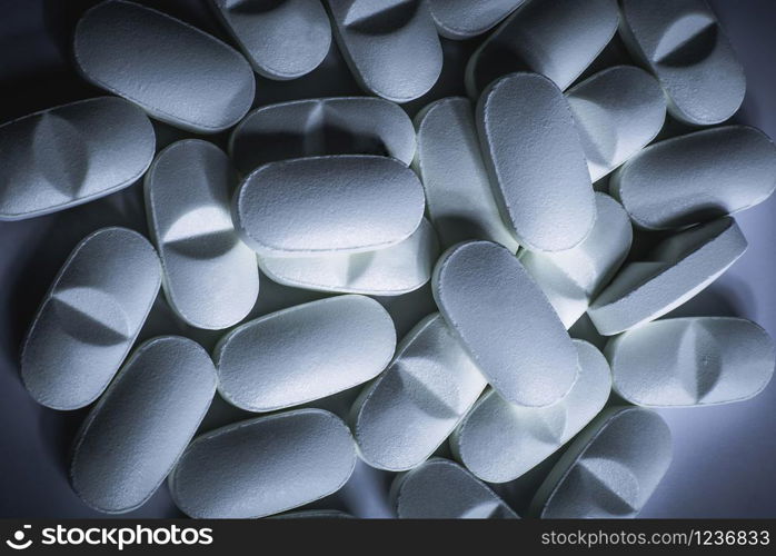Closeup of many prescription drugs, medicine tablets or vitamin pills in a pile with cool blue color tone - Concept of healthcare, opioids addiction, medicament abuse or medication treatment.