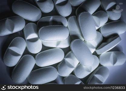 Closeup of many prescription drugs, medicine tablets or vitamin pills in a pile with cool blue color tone - Concept of healthcare, opioids addiction, medicament abuse or medication treatment.