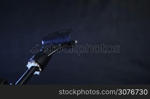 Closeup of microphone being adjusted in music stand to record guitar sound in studio against black background.