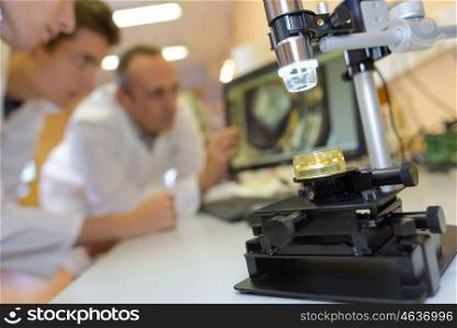 Closeup of microscope, students in background