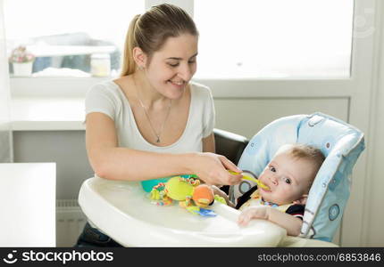 Closeup of mother giving porridge to her baby boy from plastic spoon