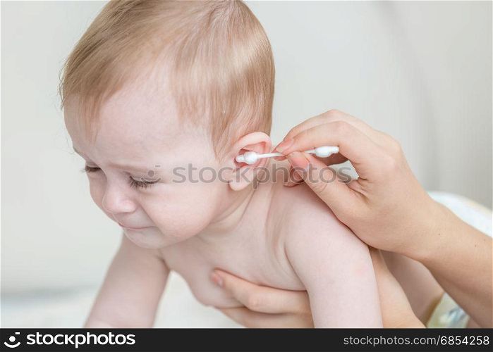 Closeup of mothers hand cleaning her baby&rsquo;s ear with cotton swab