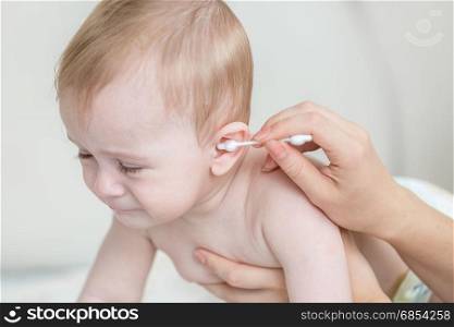 Closeup of mothers hand cleaning her baby&rsquo;s ear with cotton swab