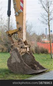 closeup of muddy excavator shovel on grass near building site