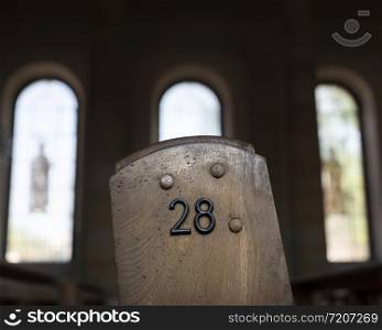 closeup of number 28 on side of old wooden church bench with roman windows in the background