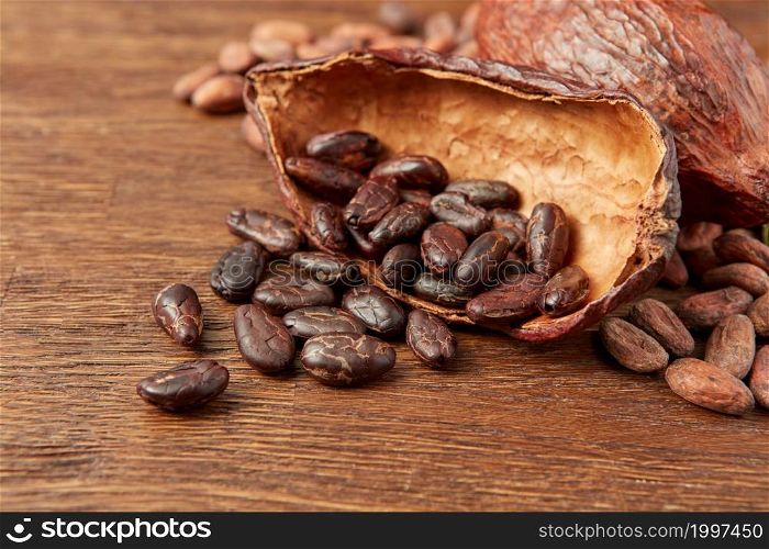 Closeup of peeled aromatic cocoa beans in half of cocoa pod composed with whole pod and unpeeled beans on wooden surface. Dark raw beans in cocoa pod