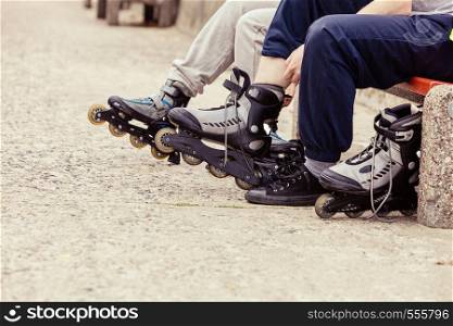 Closeup of people friends putting on roller skates outdoor. Woman and man sitting on bench.. People friends putting on roller skates outdoor.