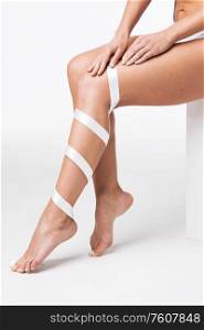 Closeup of perfect women&rsquo;s legs with white ribbon on white background. Womens legs with white ribbon