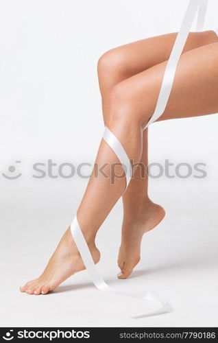 Closeup of perfect women&rsquo;s legs with white ribbon on white background. Perfect women&rsquo;s legs with white ribbon