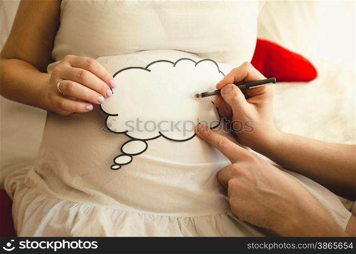 Closeup of photo of man writing on paper sign on wife&rsquo;s pregnant abdomen