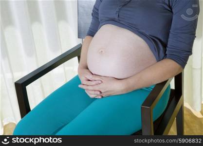 Closeup of pregnant woman at home on a chair