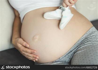 Closeup of pregnant woman holding baby socks on belly