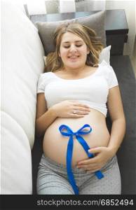 Closeup of pregnant woman holding blue bow on belly