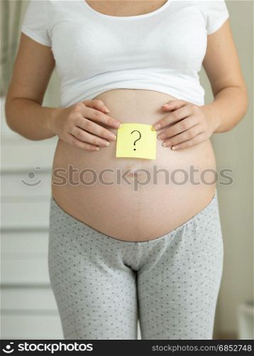 Closeup of pregnant woman holding question mark drawn on memo sticker