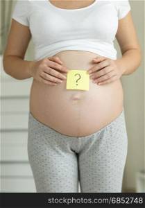 Closeup of pregnant woman holding question mark drawn on memo sticker