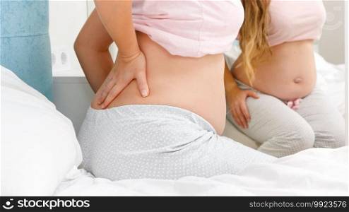 Closeup of pregnant woman massaging her aching back while stting on bed. Concept of pregnancy healthcare and medical examination. Closeup of pregnant woman massaging her aching back while stting on bed. Concept of pregnancy healthcare and medical examination.