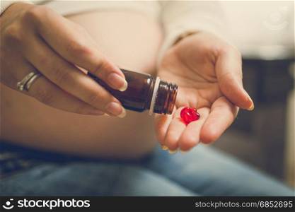 Closeup of pregnant woman on third trimester holding vitamins in pills