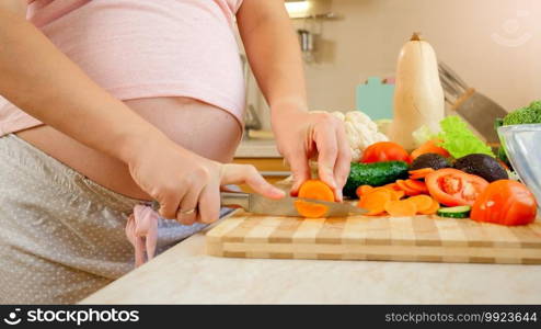 Closeup of pregnant woman with big belly cutting vegetables and cooking sald on kitchen. Closeup of pregnant woman with big belly cutting vegetables and cooking sald on kitchen.