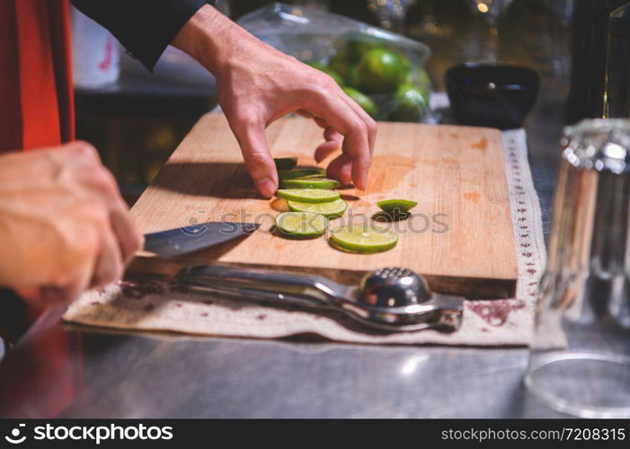 Closeup of professional bartender hand slicing lemon for making lemonade juice by knife in night club. Chef making drinks for guest in pub restaurant. Food and beverage concept.