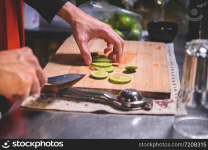 Closeup of professional bartender hand slicing lemon for making lemonade juice by knife in night club. Chef making drinks for guest in pub restaurant. Food and beverage concept.