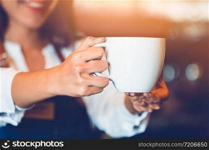 Closeup of professional female barista hand making and holding white cup of coffee. Happy young woman at counter bar in restaurant background. People lifestyles and Business occupation concept