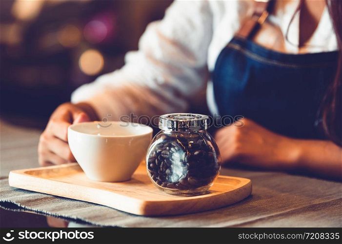 Closeup of professional female barista hand making and holding white cup of coffee. Happy young woman at counter bar in restaurant background. People lifestyles and Business occupation concept