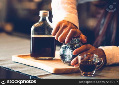 Closeup of professional female barista hand opening bottle of coffee to making cup of coffee. Happy young woman at counter bar in restaurant background. People lifestyles and Business occupation