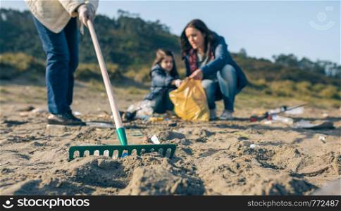 Closeup of rake with volunteer women cleaning the beach. Selective focus in rake in foreground. Rake with volunteer women cleaning the beach