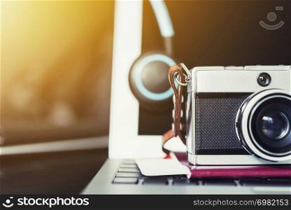 Closeup of retro film camera and headphone on passport and laptop with backlight. Photography and travel concept.