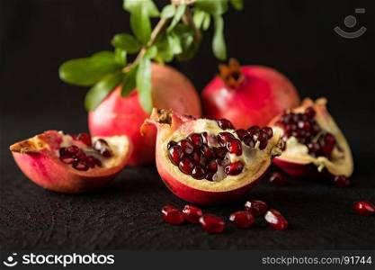 Closeup of ripe pomegranate fruits and seeds over a textured black background. Closeup of ripe pomegranate fruits and seeds