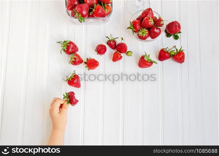 Closeup of ripe red strawberry in child&rsquo;s hands, on white wooden table. Harvest from your garden. The concept of healthy eating.. Closeup of ripe red strawberry in child&rsquo;s hands, on white wooden table. Harvest from your garden.