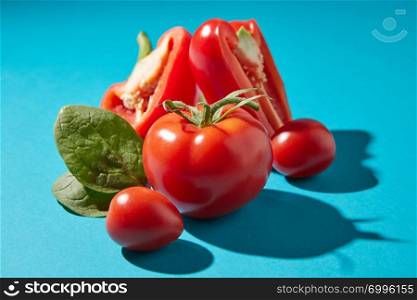 Closeup of ripe tomatoes with green stems, pepper halves and fresh spinach leaves on a blue background with reflection of the shadows and space for text. Vegetarian food. Closeup of organic spinach leaves, peppers and tomatoes on a dark blue background with copy space and reflection of shadows. Healthy ingredients for dietary salad.