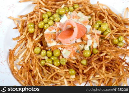 Closeup of salad with salmon fish at fried sliced potato with carrot and peas dressed by tomato sauce with cognac