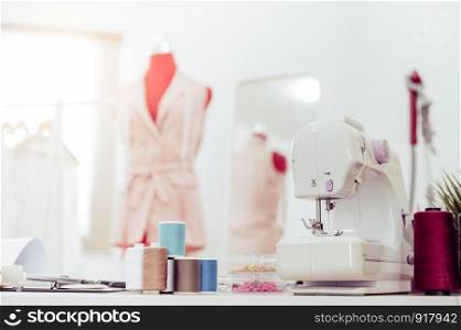 Closeup of sewing machine with fashion designer showroom studio workshop background with new collection of pink pastel female clothes design. Tailor and sewing concept. Dressmaker modern room interior
