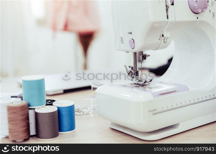 Closeup of sewing machine with fashion designer showroom studio workshop background with new collection of pink pastel female clothes design. Tailor and sewing concept. Dressmaker modern room interior