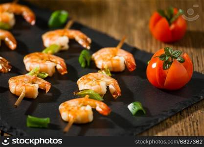 Closeup of shrimp skewers with tomatoes and herbs on a stone. Closeup of shrimp skewers with tomatoes and herbs