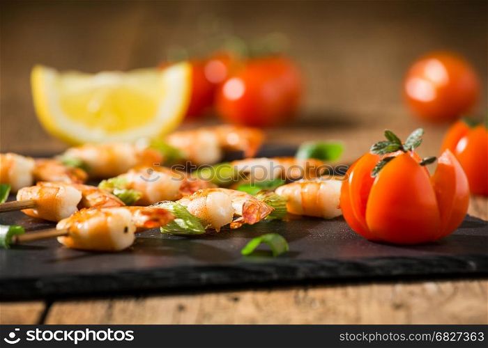 Closeup of shrimp skewers with tomatoes and herbs on a stone over an old wooden table. Closeup of shrimp skewers with tomatoes and herbs on a stone