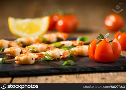 Closeup of shrimp skewers with tomatoes and herbs on a stone over an old wooden table. Closeup of shrimp skewers with tomatoes and herbs on a stone